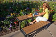 a woman is sitting on a bench in front of flowers with a book and laptop