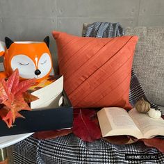 an orange fox pillow sitting on top of a couch next to a book