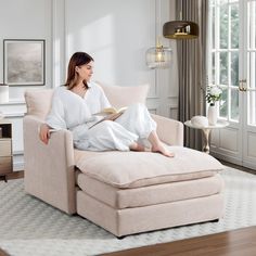 a woman sitting on a chair reading a book in a living room with white walls