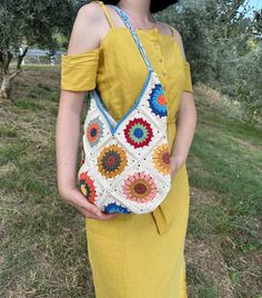 a woman in a yellow dress is holding a crocheted purse