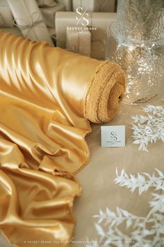 a roll of shiny gold fabric next to a glass vase