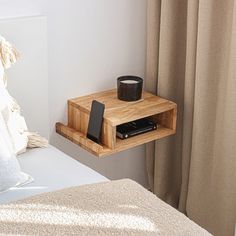 a small wooden shelf on the side of a bed with a cell phone and cup