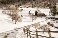 a snow covered field with a house in the background and a wooden fence around it