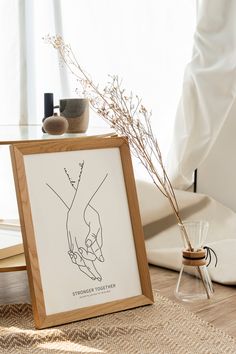 a wooden frame with a drawing of two hands holding each other's hand next to a coffee table