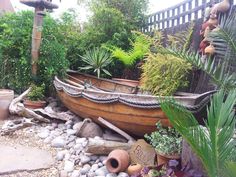 a wooden boat sitting on top of a pile of rocks next to trees and plants