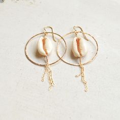 "Beautiful sliced cowrie shells hang within gold filled hammered hoops and have delicate gold chains dangling from them. Hoops measure approximately 1 1/2\". Each cowrie shell is unique so please allow for variations." Beach Jewelry With Dangling Charms, Bohemian 14k Gold Filled Jewelry For Beach, Bohemian Gold Hoop Earrings With Dangling Charms, Handmade 14k Gold Filled Jewelry For The Beach, Gold Shell-shaped Hoop Earrings For Beach, Handmade 14k Gold Filled Beach Earrings, Handmade Gold Hoop Earrings For Vacation, Handmade 14k Gold Filled Earrings For Beach, Handmade 14k Gold-filled Earrings For Beach