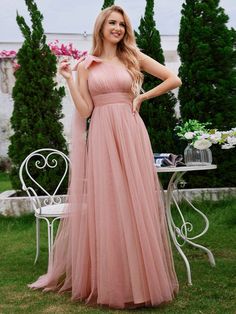 a woman standing in front of a table wearing a pink dress and holding a flower