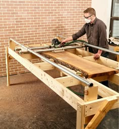 a man working on a wooden table with metal pipes and wood planks in front of a brick wall