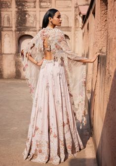 Presenting an off-white Chikankari mukaish lehenga adorned with pearl and zardozi hand embroidery. Paired seamlessly with a sheeted crystal bustier choli and an organza cutwork border-embroidered dupatta. This ensemble exudes timeless elegance, combining traditional craftsmanship with modern flair. Traditional Embroidered Pre-draped Saree With Cape Sleeves, Anarkali Pre-draped Saree With Sheer Dupatta And Cape Sleeves, Traditional Embroidered Anarkali Set With Cape Sleeves, Designer Dresses With Intricate Embroidery And Cape Sleeves, Anarkali Pre-draped Saree With Zari Work And Cape Sleeves, Eid Dresses With Resham Embroidery And Cape Sleeves, Fitted Gown With Dupatta And Cape Sleeves, Fitted Embroidered Anarkali Set With Cape Sleeves, Anarkali Gown With Cape Sleeves And Resham Embroidery