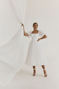 a woman in a white dress is holding curtains