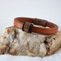 two leather bracelets sitting on top of a rock in the snow with white background