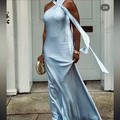 a woman in a long blue dress is standing on the sidewalk wearing a gold purse