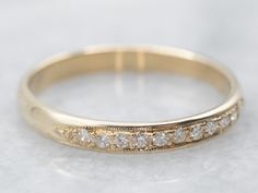 a gold wedding ring with five diamonds on it's side, sitting on a white surface