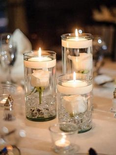 two clear vases filled with white flowers and lit candles