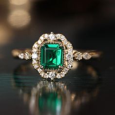 an emerald and diamond ring on a table