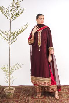 A maroon, raw silk, Kashmiri cut long kurta with Marori lace on the neck and sleeves. A pink tissue silk ajar pant lends a royal look to the suit. Finished with a matching tissue organza dupatta with pink border. 3-piece suit Ready to wear Eid Slub Silk Sets With Embroidered Border, Elegant Raw Silk Salwar Kameez With Embroidered Border, Silk Kurta With Embroidered Border For Eid, Traditional Long Sleeve Tissue Silk Churidar, Embroidered Tissue Silk Set For Eid, Designer Silk Sets With Embroidered Border, Elegant Red Palazzo Set With Embroidered Border, Eid Tissue Silk Sharara With Embroidered Border, Festive Unstitched Cotton Silk Suit With Embroidered Border