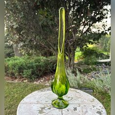 a green glass vase sitting on top of a stone table in front of a tree