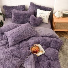 a bed covered in purple fluffy blankets and pillows