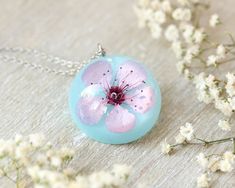 This cherry flower necklace is made from a real cherry flower picked up from the place where I live. A unique sakura necklace as the most unique birthday gift idea for women. In general, a cherry flower necklace (japanese flower necklace) is an outstanding full of significance complement for you. This sakura blossom necklace is part of my pale pink jewelry. The hypoallergenic stainless steel and the high-gloss crystalline resin gives this cherry flower necklace a precious and enamelled look. Use Spring Flower-shaped Jewelry Gift, Delicate Spring Necklaces For Gifts, Spring Flower Jewelry Gift, Delicate Necklace For Spring Gift, Spring Flower Decorated Jewelry Gift, Spring Flower Decoration Jewelry Gift, Gift Flower Pendant Necklace With Flower Decoration, Pink Round Necklace For Mom, Blossom Colored Flower Pendant Jewelry Gift