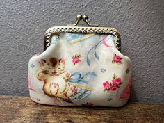 a small purse with a kitten on it sitting on a wooden table next to a gray wall