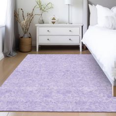 a white bed sitting next to a purple rug on top of a hard wood floor