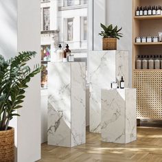 three white marble vases sitting on top of wooden floor next to a plant in a pot