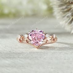 a pink diamond ring sitting on top of a white stone table next to a pine tree