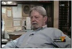 an older man sitting in front of a desk with papers on the wall behind him