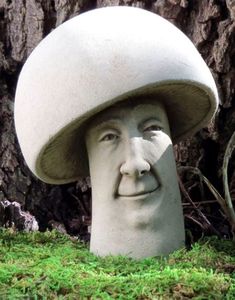 a statue of a man's head wearing a large mushroom like hat in front of a tree