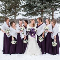 a group of women standing next to each other in the snow wearing purple dresses and fur stoles