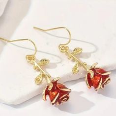 two red flowers are hanging from gold plated earwires on a white surface