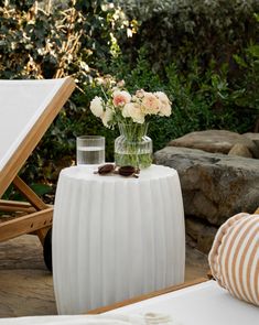 a vase with flowers sitting on top of a white table next to a beach chair