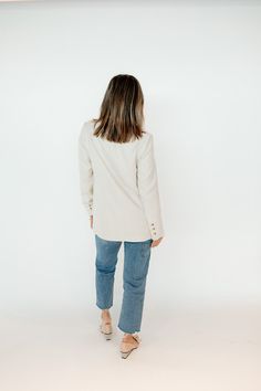 a woman standing in front of a white wall wearing jeans and a blazer jacket