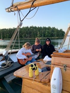 three people are sitting on the deck of a sailboat playing guitar and drinking beer