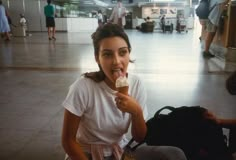 a woman sitting on the floor eating something with her mouth open and people in the background