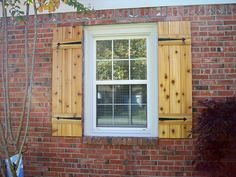 a window with shutters on the side of a red brick building next to a tree