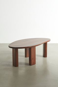 an oval wooden table sitting on top of a cement floor next to a white wall