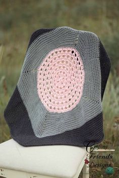 a crocheted blanket sitting on top of a white chair in the middle of a field