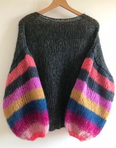 a knitted sweater hanging on a wooden hanger with two colorful striped sleeves that are open