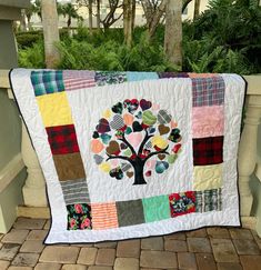 a quilted tree with hearts on it is sitting on a bench near some trees