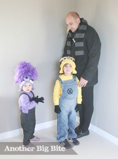 a man standing next to two small children wearing costumes and wigs on their heads