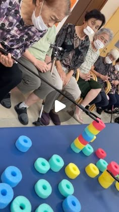 an elderly woman is playing with toys while others watch from the sidelines in front of her