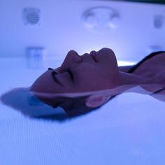 a woman laying on top of a white bed in a room with blue light coming from the ceiling