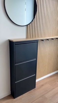 a black filing cabinet sitting next to a round mirror on the side of a wall