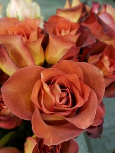 a bouquet of orange and red roses in a vase on a table with other flowers