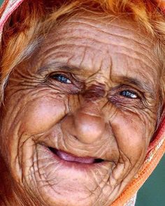 an old woman with wrinkles on her face and hood over her head is smiling at the camera