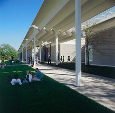 people sitting on the grass under an awning in front of a building with columns