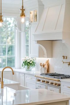 a kitchen with white cabinets and marble counter tops, gold faucets, and hanging lights