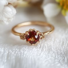 a close up view of a ring with a red stone in the center and two white flowers behind it