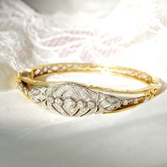 An astounding Edwardian era diamond cluster hinge bangle bracelet in 14k yellow gold and platinum. Features an ornate diamond-encrusted platinum navette setting mounted on a tapered gold band with cutout embellishments and a latch box clasp. Built into the focal point of this bracelet is 5 round-cut diamonds secured in a horizontal line of bezel settings. The open work on either side of the platinum setting is also decorated with three prong-set diamond accents. All the diamonds seem to be in go Vintage White Gold Diamond Bracelet With Brilliant Cut, Formal Diamond Cuff Bracelet Fine Jewelry, Formal Diamond Cuff Bracelet With Diamond Accents, Vintage Brilliant Cut Diamond Bracelet For Wedding, Elegant Oval Hallmarked Bangle, Elegant Diamond Cut Cuff Bracelet For Anniversary, Elegant Hallmarked Cuff Bracelet For Anniversary, Luxury Gold Bangle With Rose Cut Diamonds, Formal Cuff Bracelet With Intricate Design